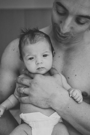 Black and white portrait of infant resting against parent's chest.