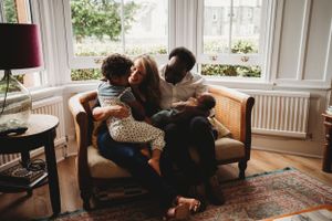 Cozy family scene on brown leather couch in sunlit living room with large windows.