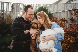 Family outdoor portrait with their golden doodle dog and swaddled newborn in autumn setting.