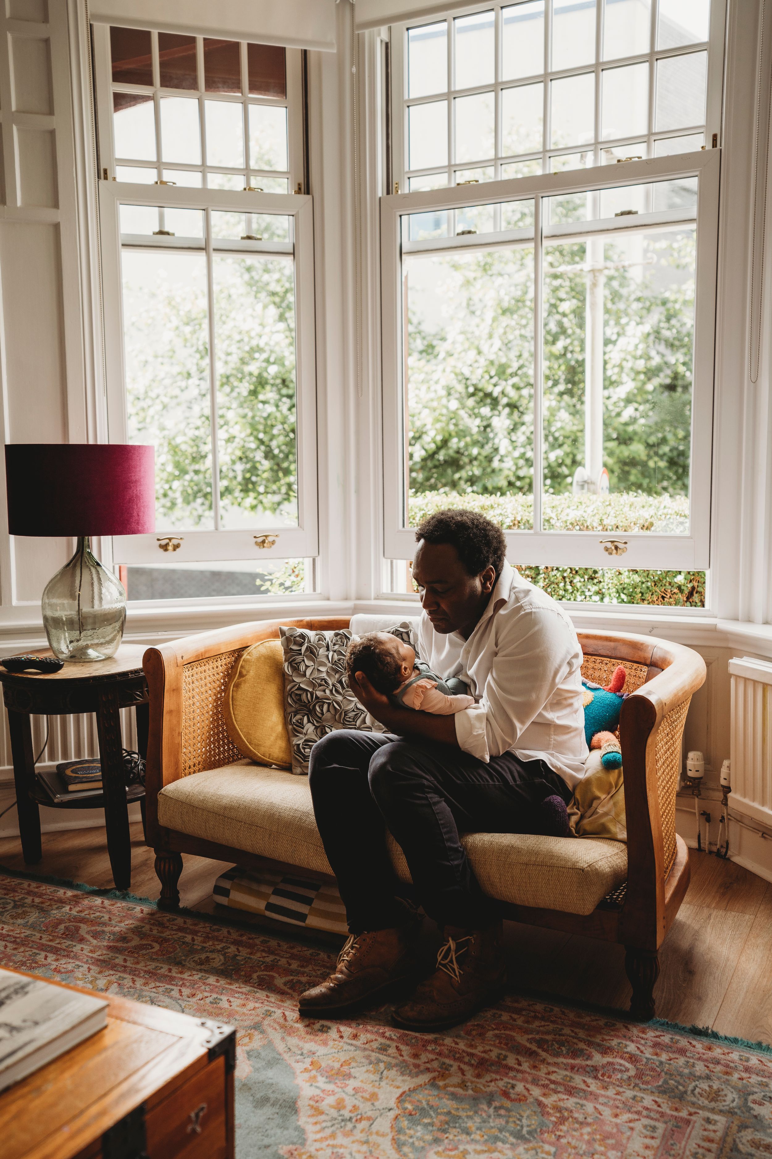 Peaceful parenting moment in sunlit living room with vintage furniture and large windows.