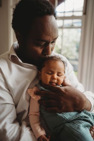 Tender moment between parent and sleeping baby in soft natural window light.