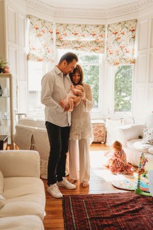Bright living room scene with family and child playing near bay window with floral curtains.