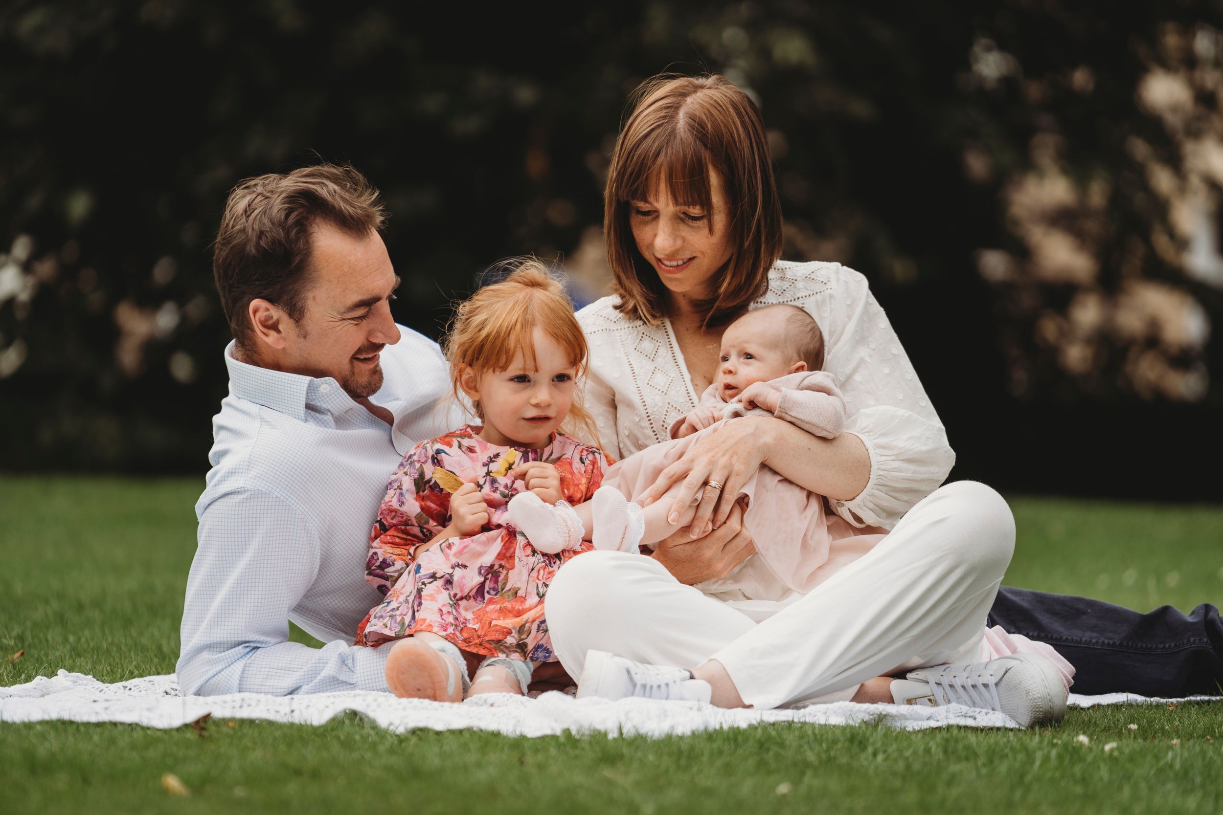 Family picnic scene on grass with white blanket during outdoor photoshoot.