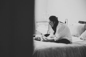 Black and white image of parent and baby resting on bed.