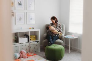 A nursery room with a green ottoman features framed wall art and a peaceful moment with a baby.