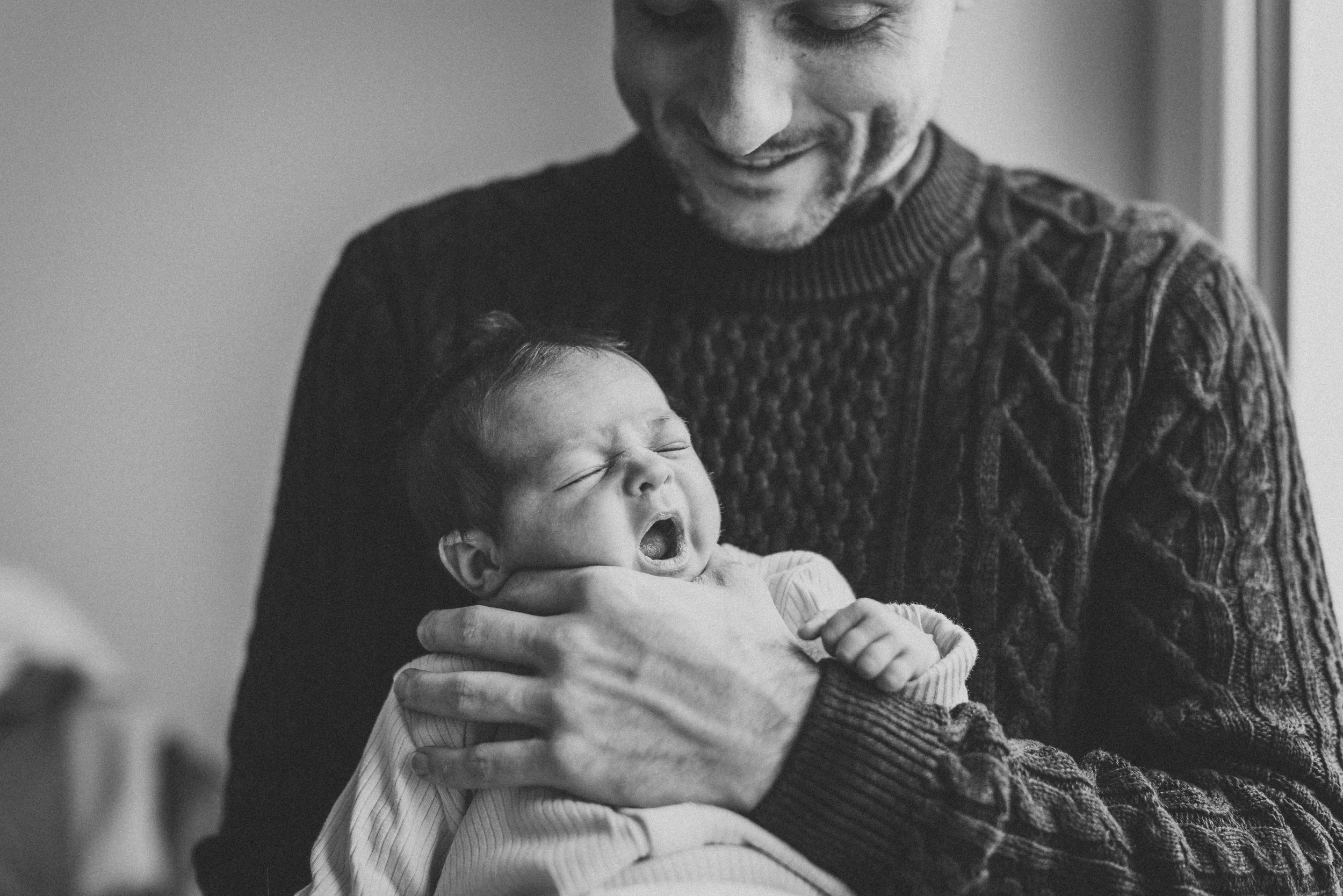 Black and white image showing tender moment of comfort with a yawning newborn.