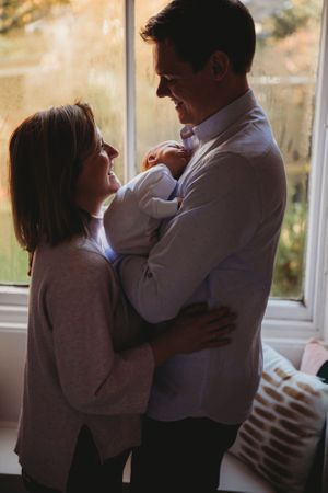 A tender family moment by a sunlit window as they admire their newborn.