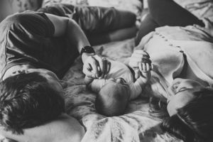 Black and white photograph of a family sharing an intimate moment on bed linens.