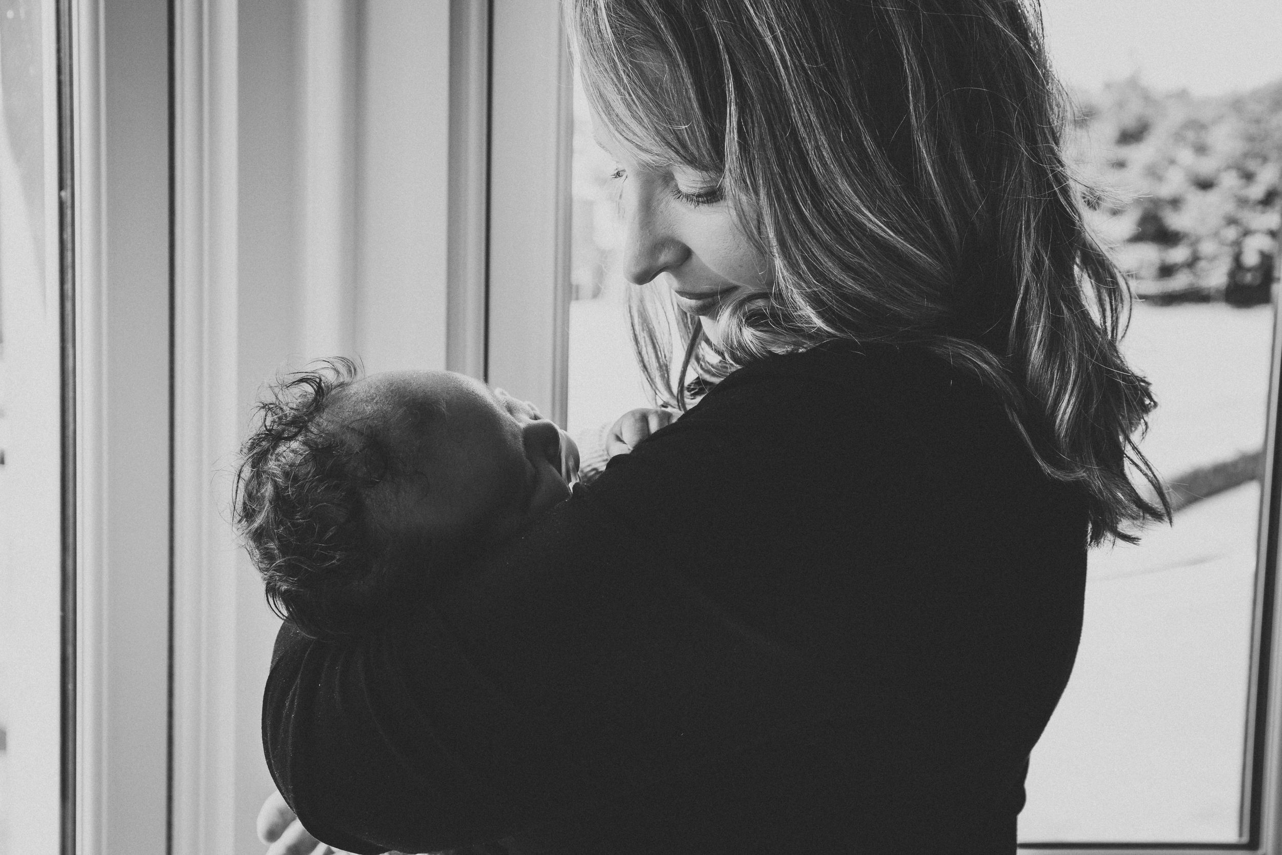 Black and white portrait capturing intimate bonding moment by window with newborn.