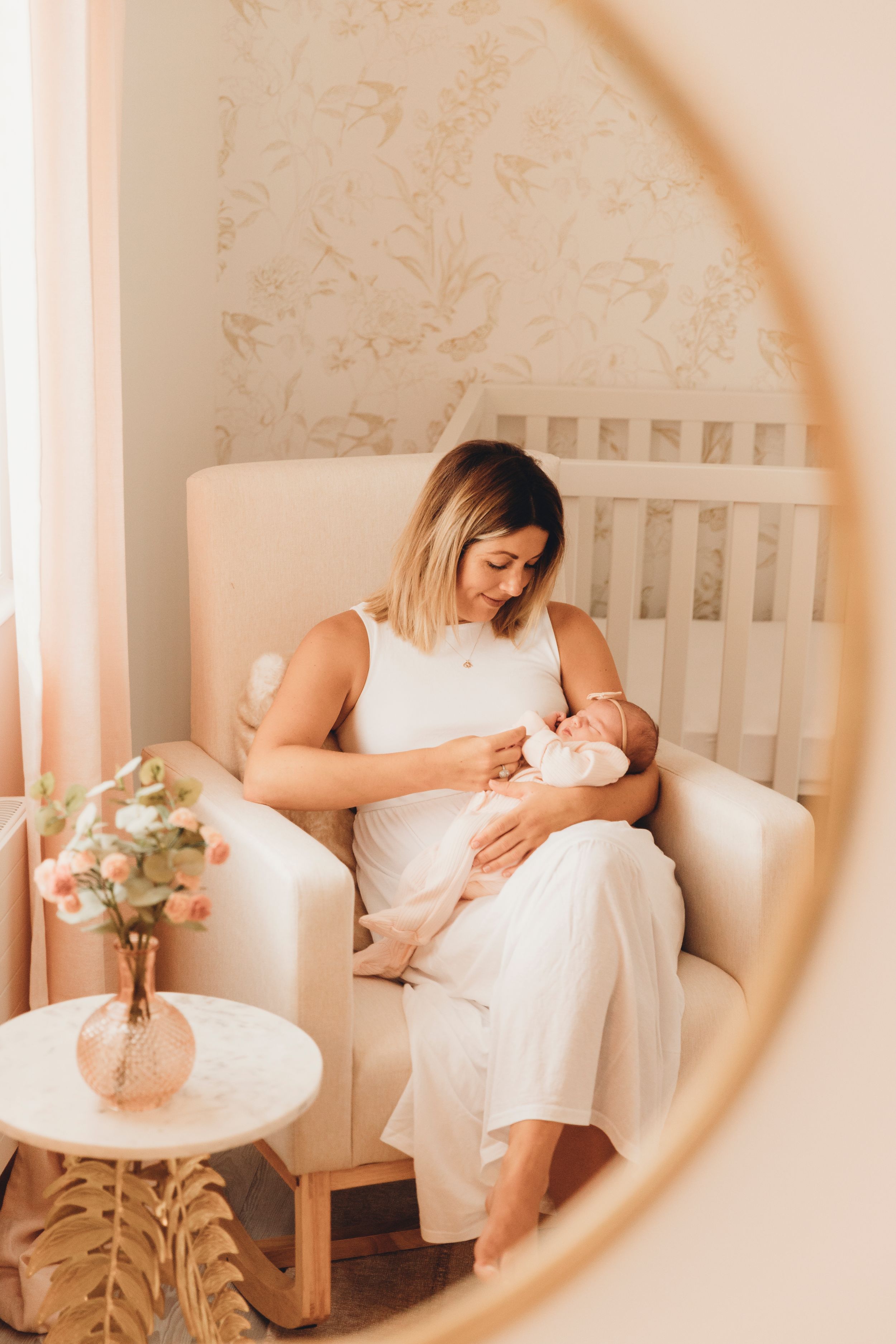A peaceful nursery scene showing a tender moment of bonding in a white chair with soft decor and flowers.