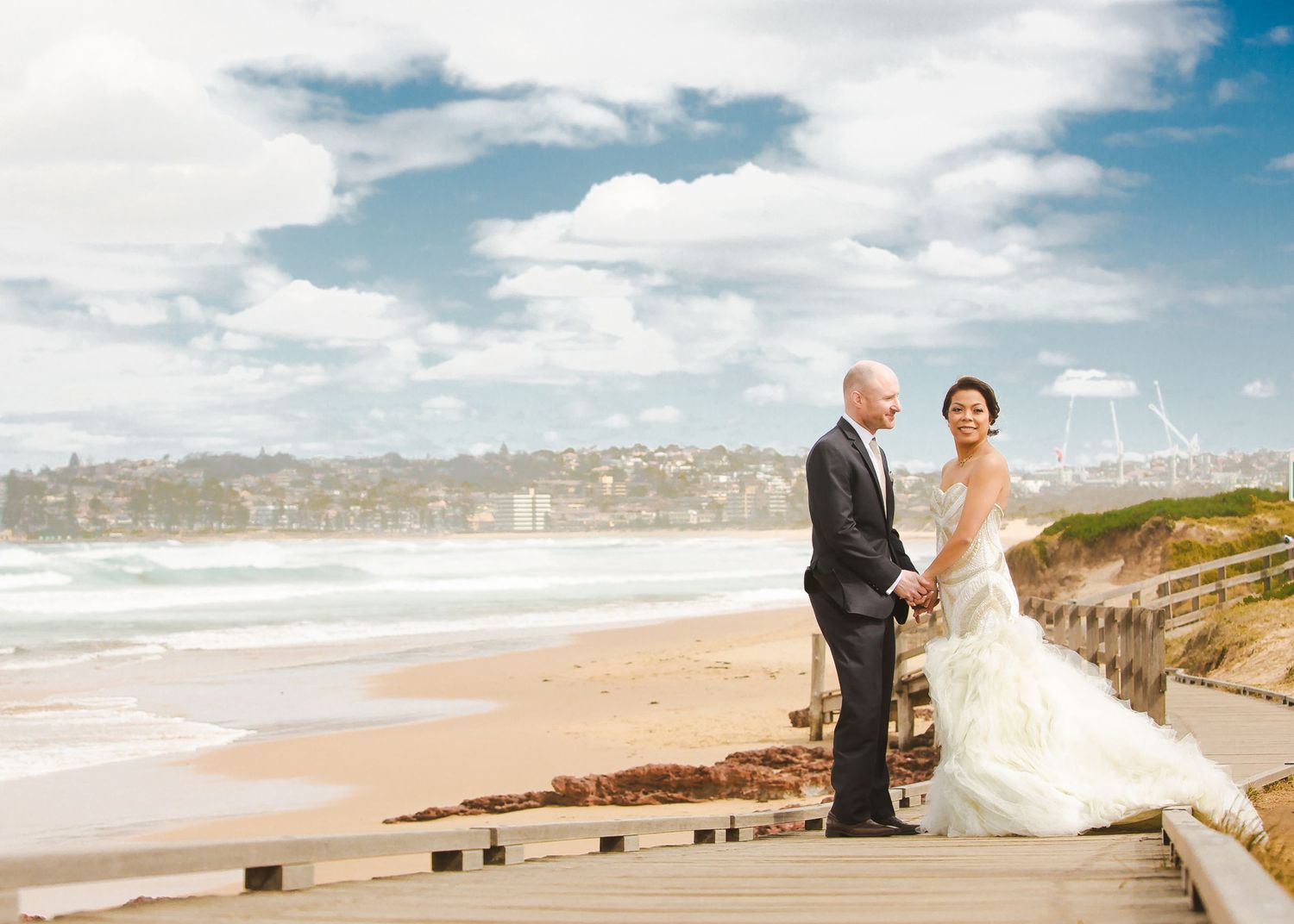 Bride and groom holding hands on a coastal boardwalk, captured by destination wedding photographer.