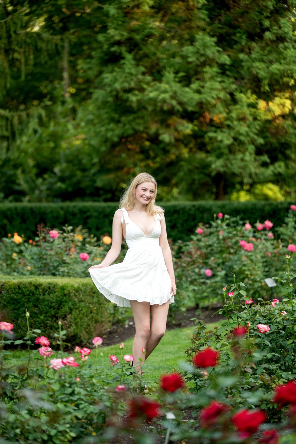 Blonde woman in white dress walking through colorful rose garden.