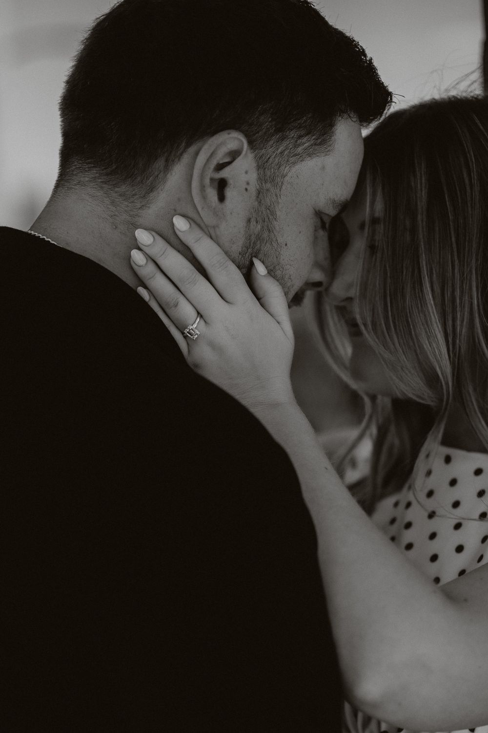 Black and white photo of a couple sharing an intimate moment, woman with engagement ring gently holding mans face.