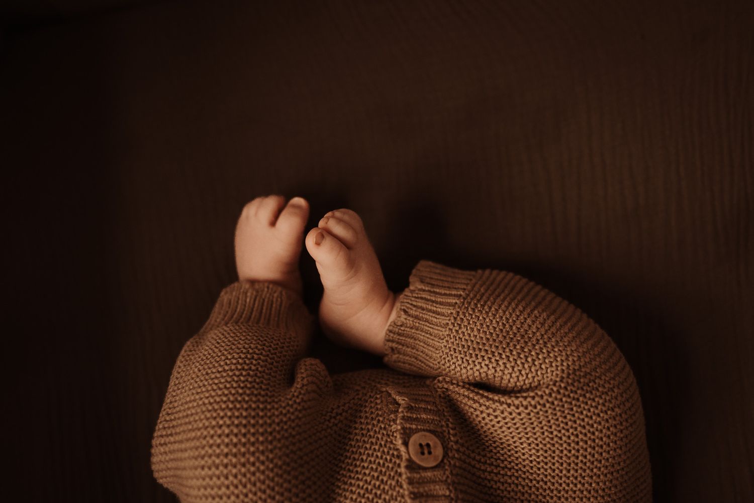 A couple lounges together on a brown leather couch holding their newborn during a newborn session