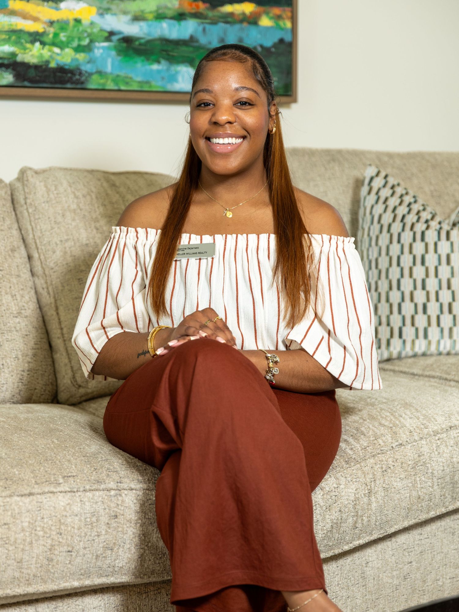Smiling woman in striped off-shoulder top holding pink tablet, seated in modern kitchen.