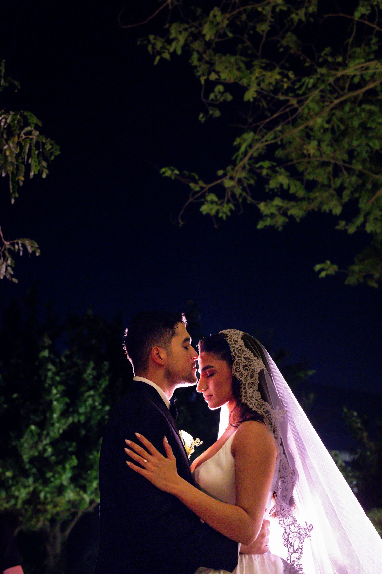 Black and white wedding photo of bride and groom sharing an intimate moment, holding hands in dramatic lighting.