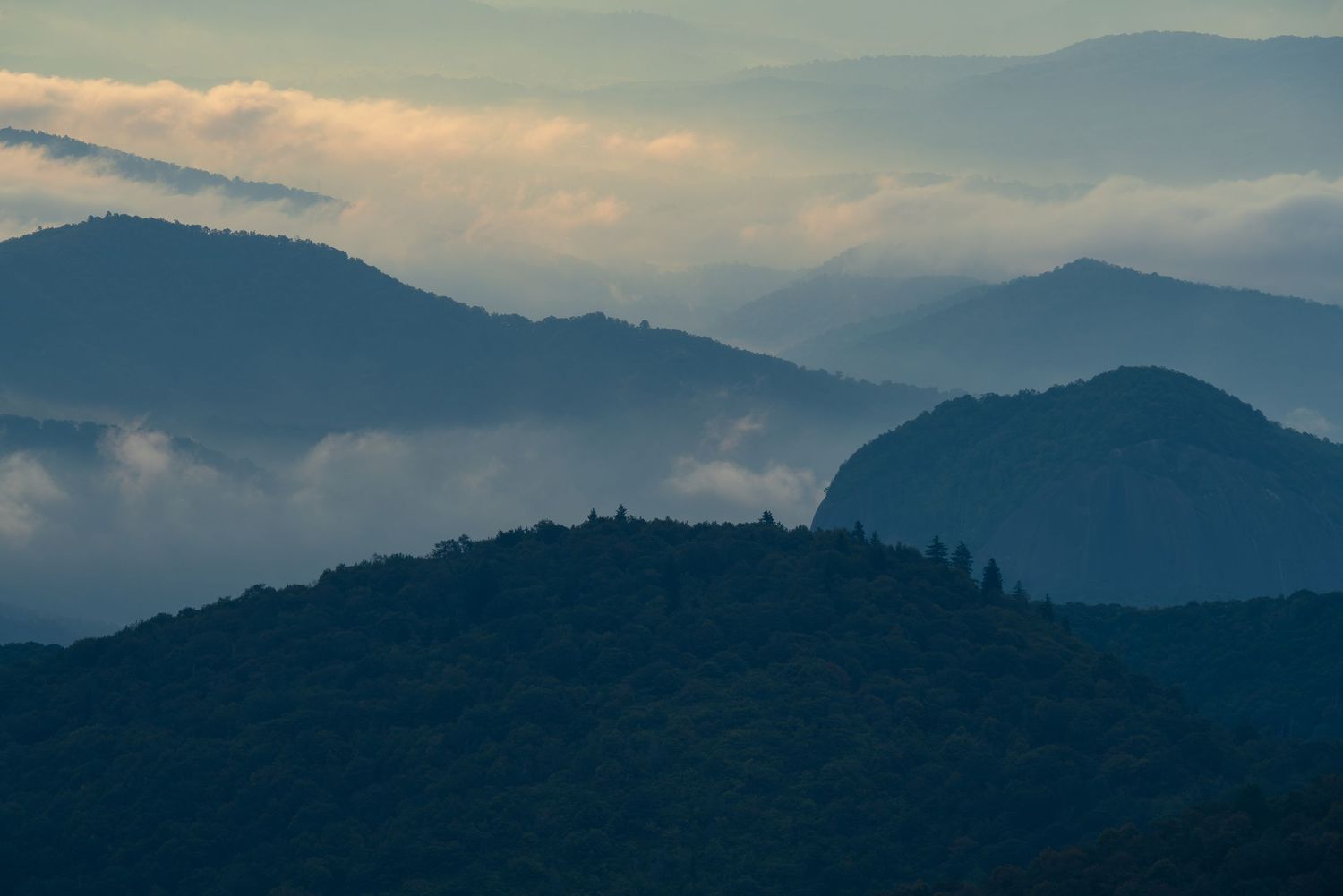 Misty blue mountain layers with low clouds at dusk, creating a serene atmospheric landscape with silhouetted ridgelines.