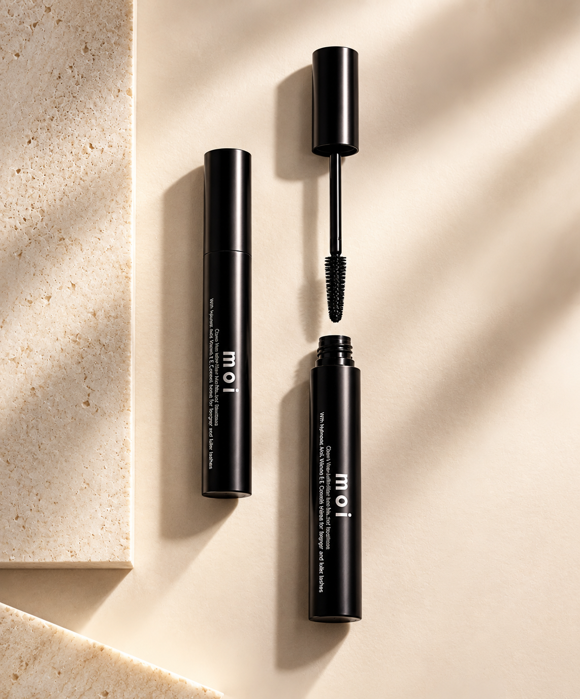 Two black MOI mascara tubes on a beige surface, one open showing the wand applicator.