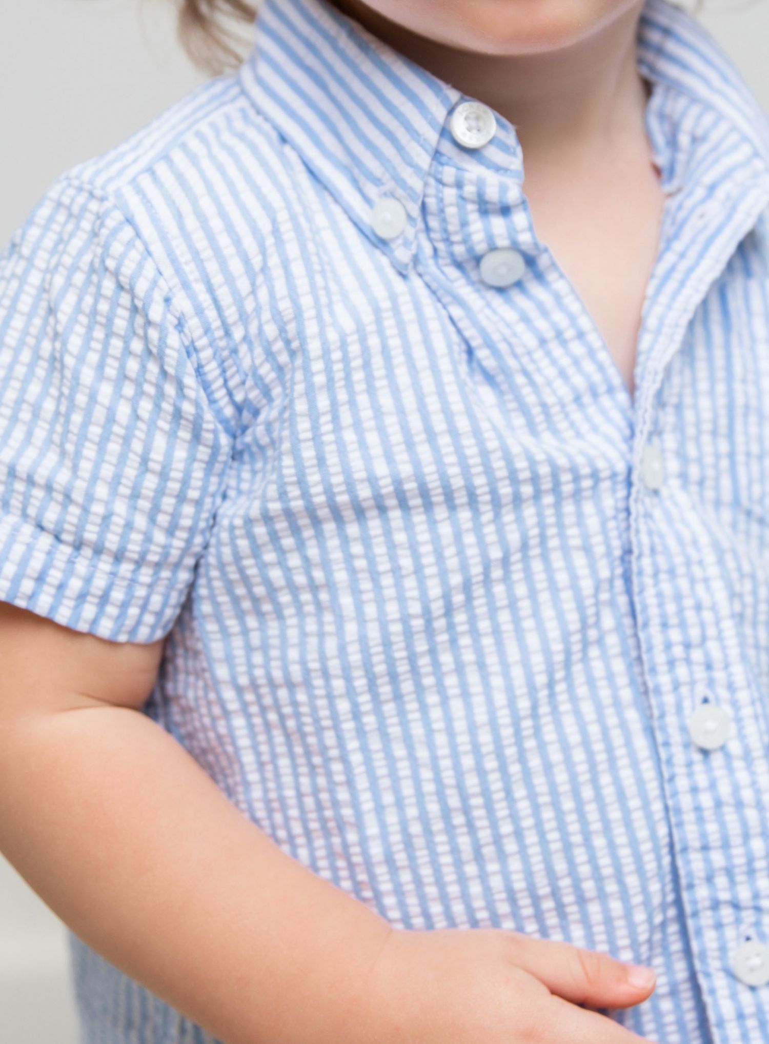 Close-up of a child wearing a blue and white striped seersucker short-sleeve button-up shirt.