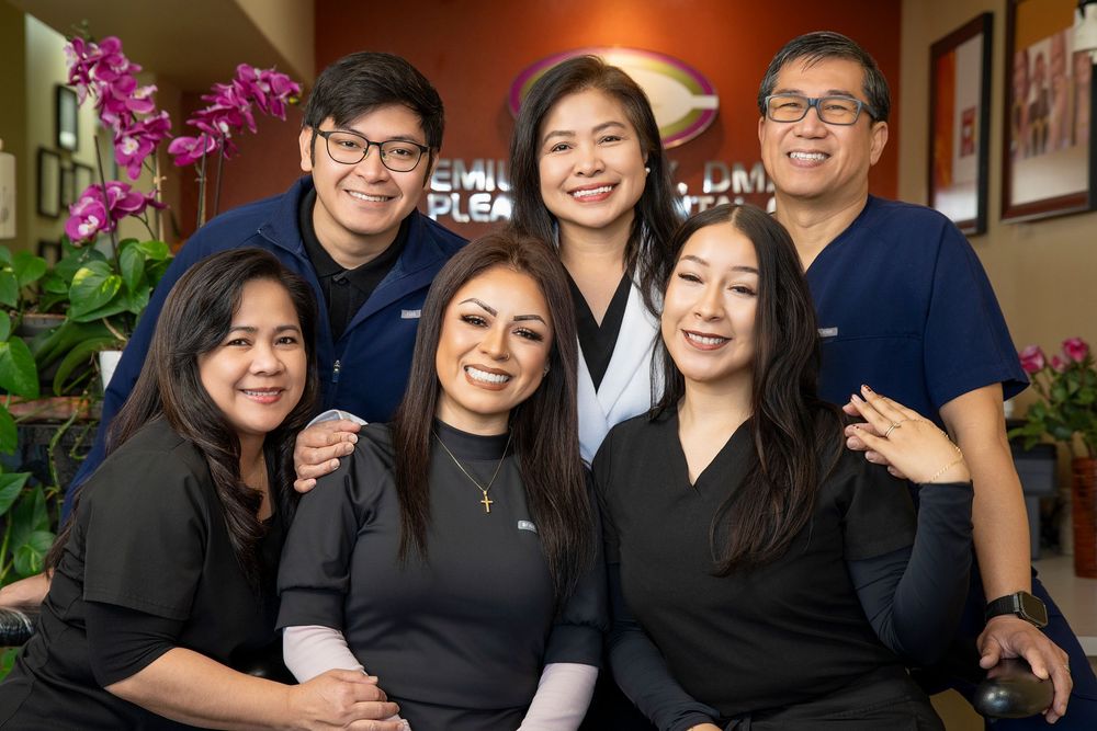 Smiling dental team of six staff members posing together in a modern dental office with purple orchids in the background.