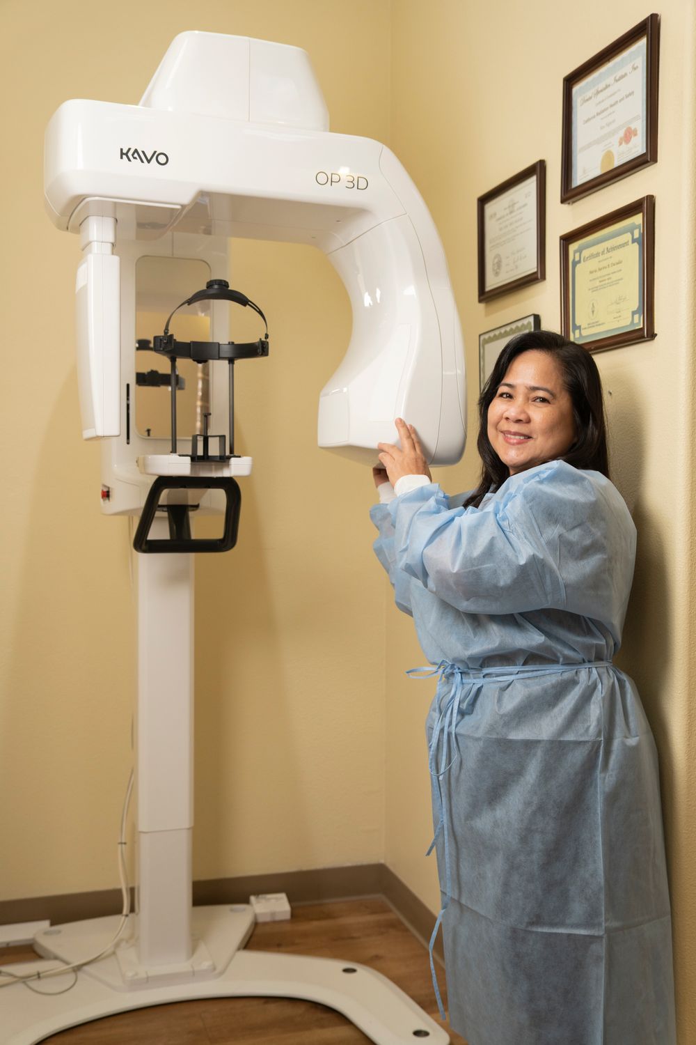 Dental professional in blue scrubs operating a KaVo OP 3D panoramic X-ray machine in a modern dental office.