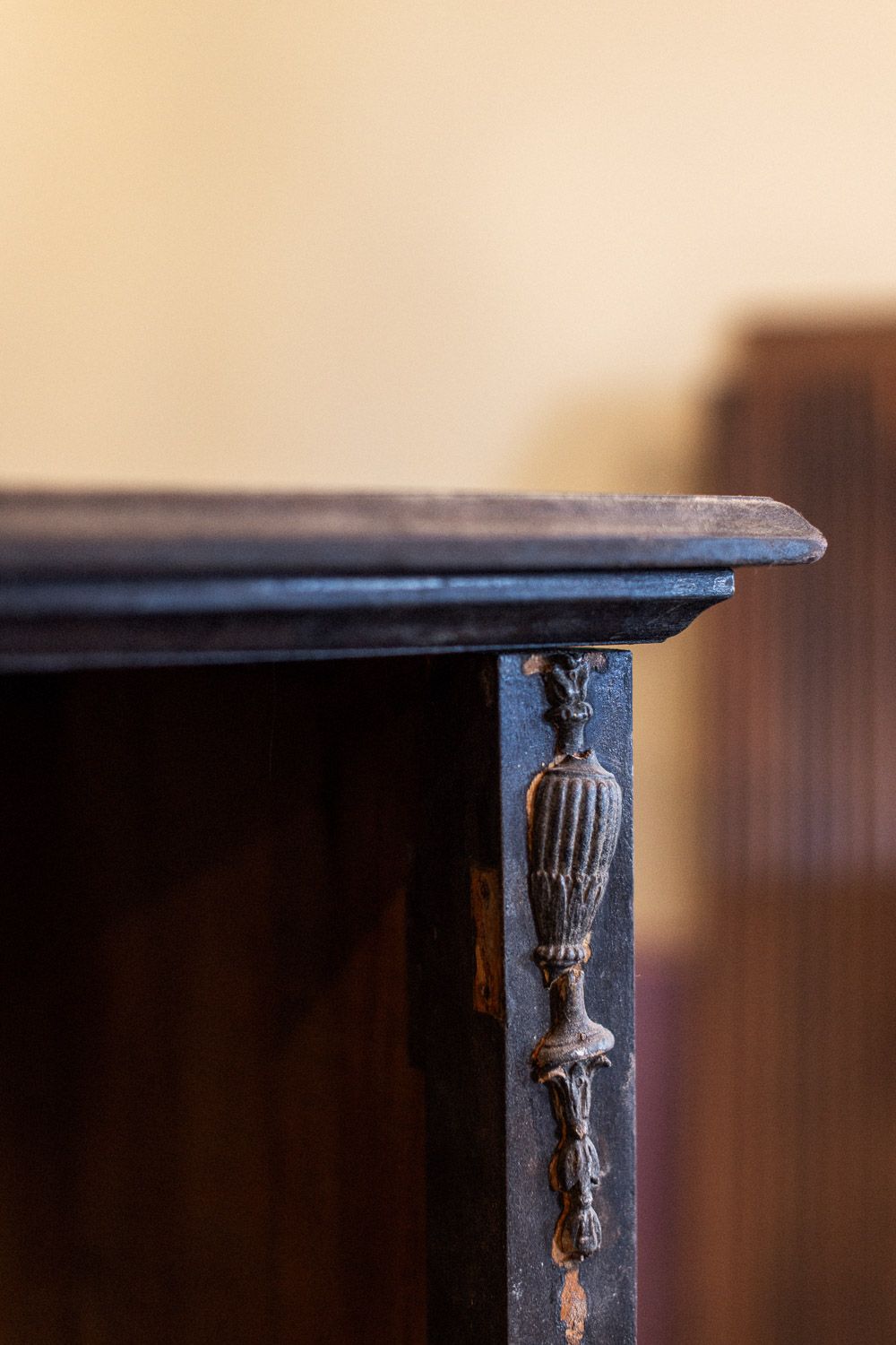 Close-up of an antique dark wood furniture corner with ornate carved urn detail on the leg.