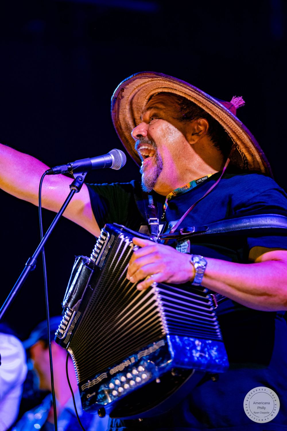 Musician playing accordion and singing into microphone while wearing a sombrero hat on stage.