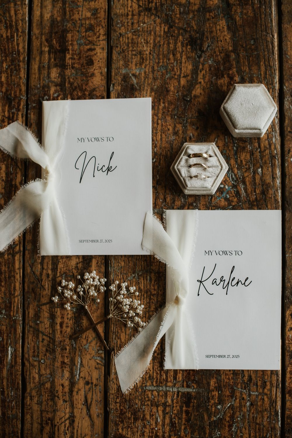 Elegant wedding vow booklets for Nick and Karlene dated September 27, 2021, with white ribbon and a velvet ring box on rustic wood.
