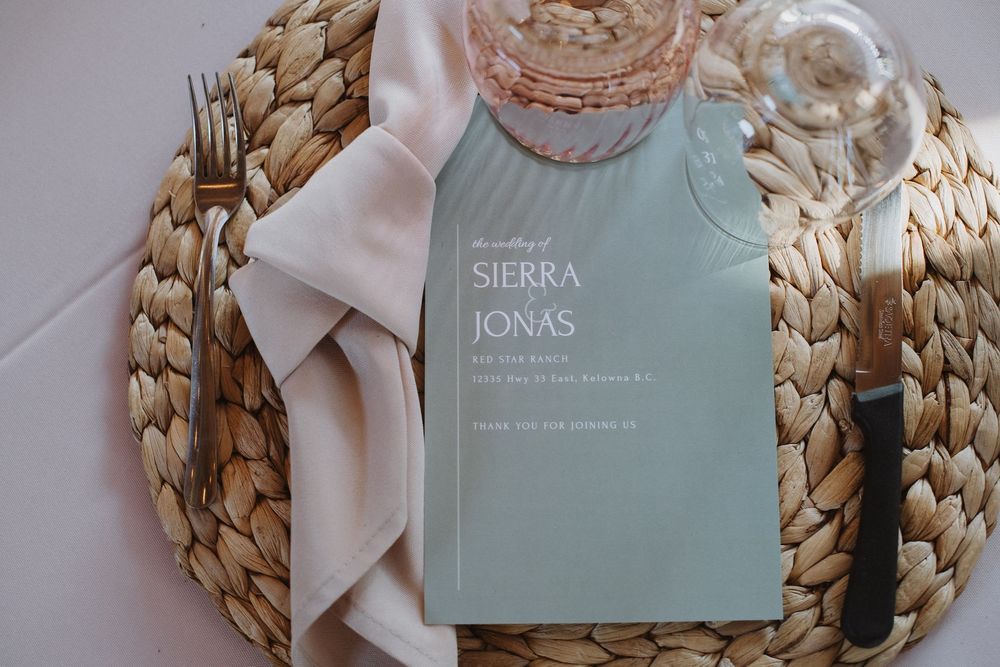 Elegant wedding menu card for Sierra and Jonas on a woven placemat with linen napkin, fork, and knife.