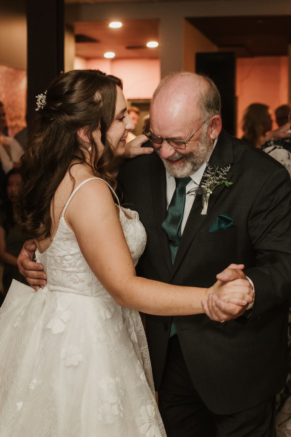Bride and father sharing an emotional first dance at wedding reception, smiling and holding hands.