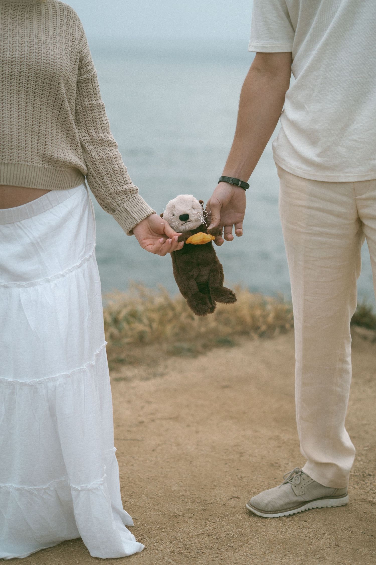 Pregnant woman in black dress holding white baby's breath flowers while cradling her baby bump outdoors.