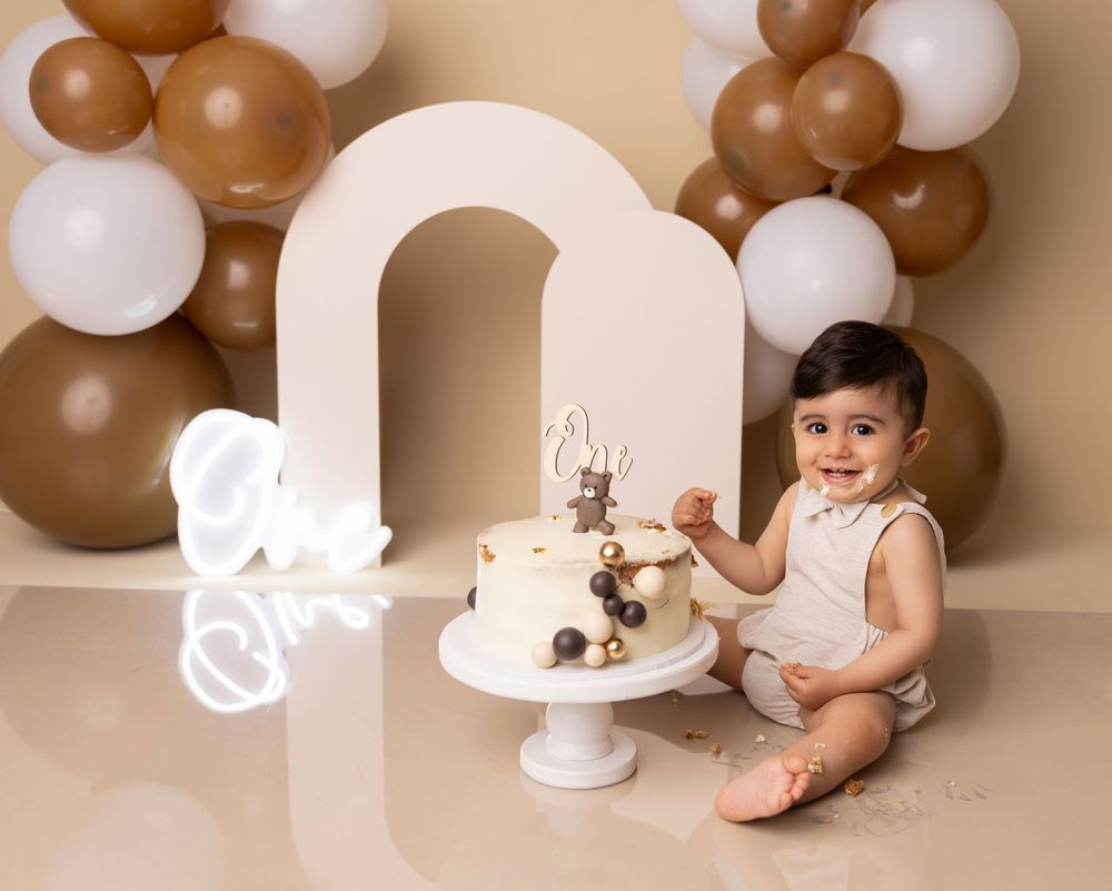 Baby's first birthday cake smash with brown and white balloon arch on beige backdrop.