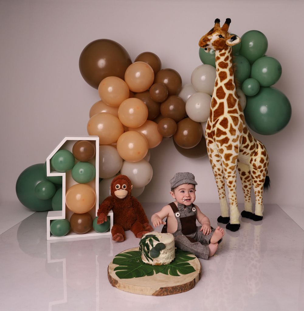 Baby's first birthday safari smash cake setup with giraffe, monkey, number one, and colorful balloon garland.
