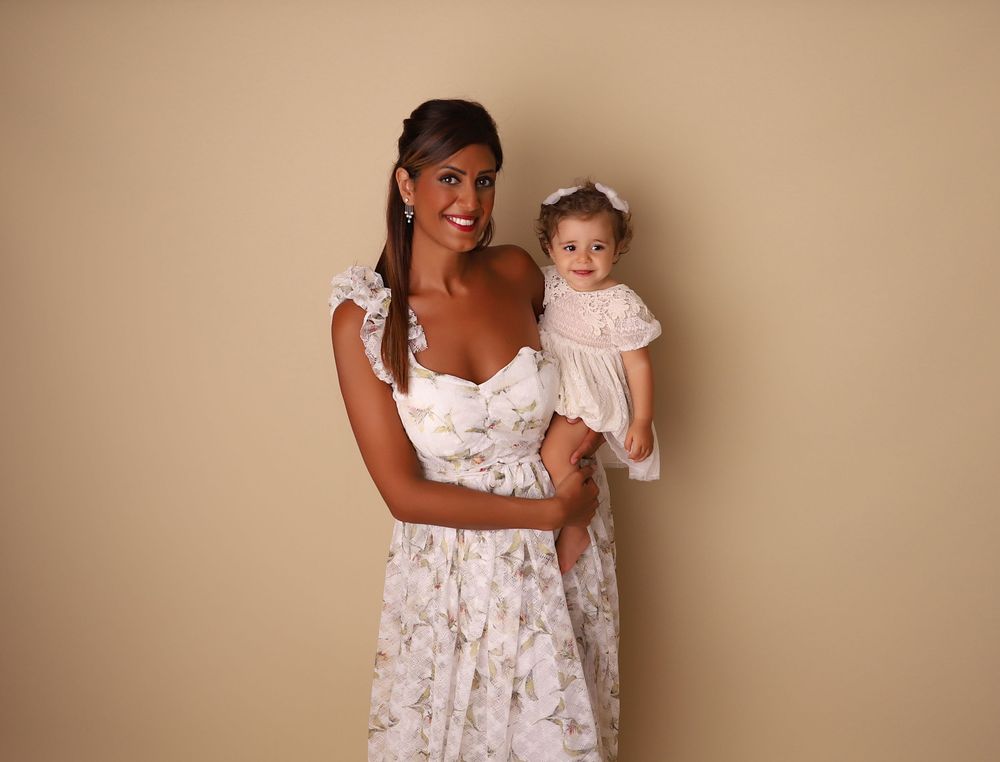Woman in floral dress holding a baby girl in pink outfit against beige background.