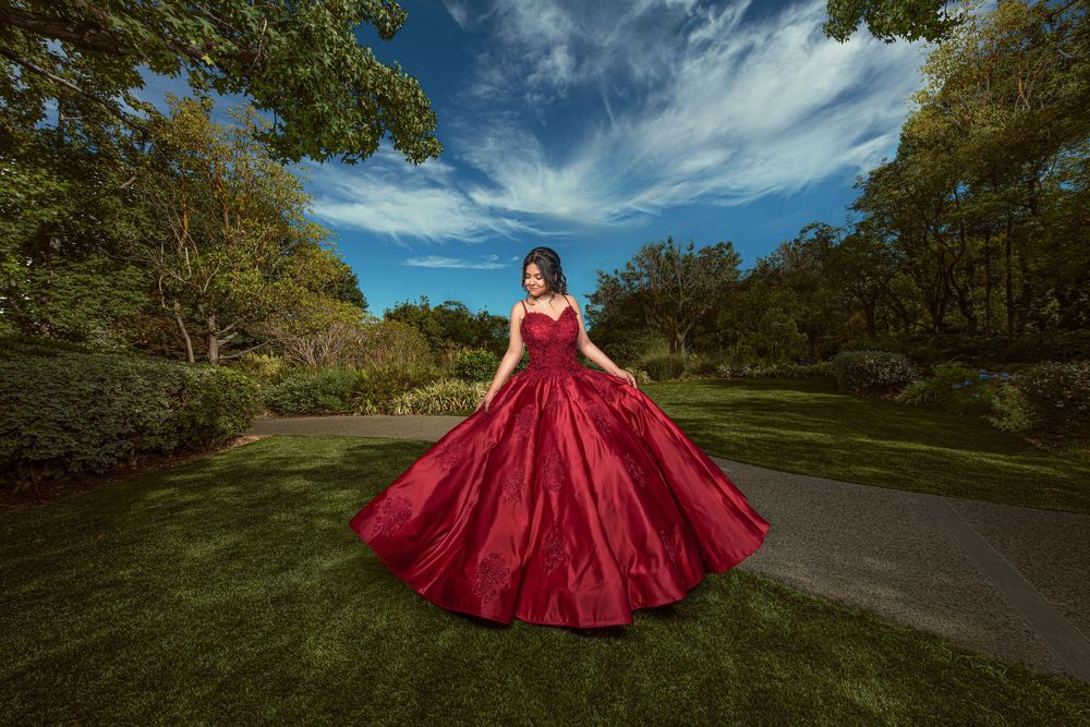 Woman in red ballgown posing in lush green park under blue sky.