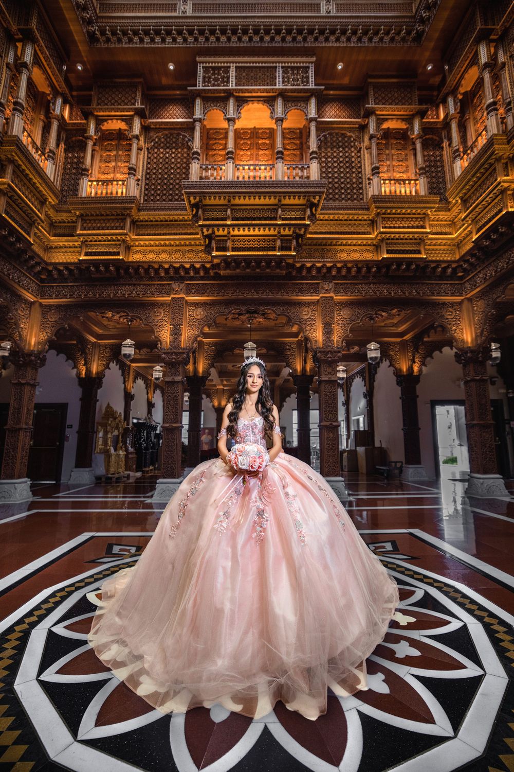 A woman in a pink ballgown stands in an ornate golden palace hall with intricate carved architecture and marble floors.