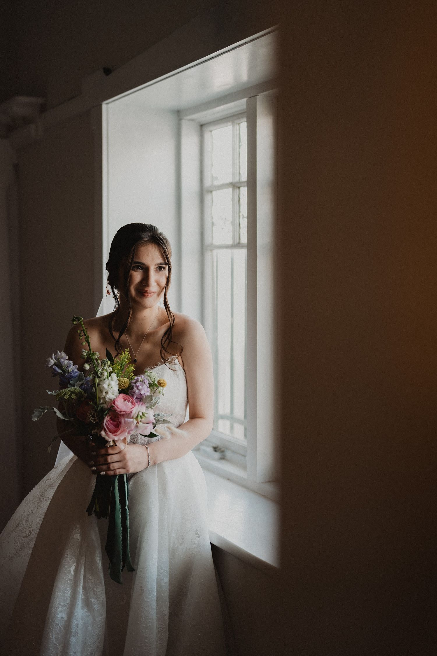 Bride holding her bouquet in soft window light