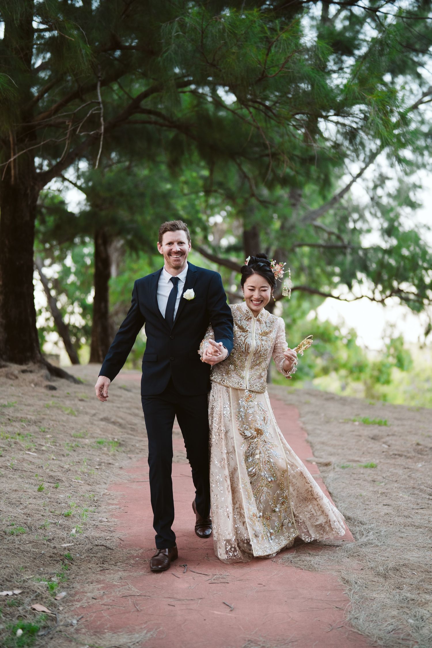 Bride and groom walking hand in hand along a tree-lined garden path