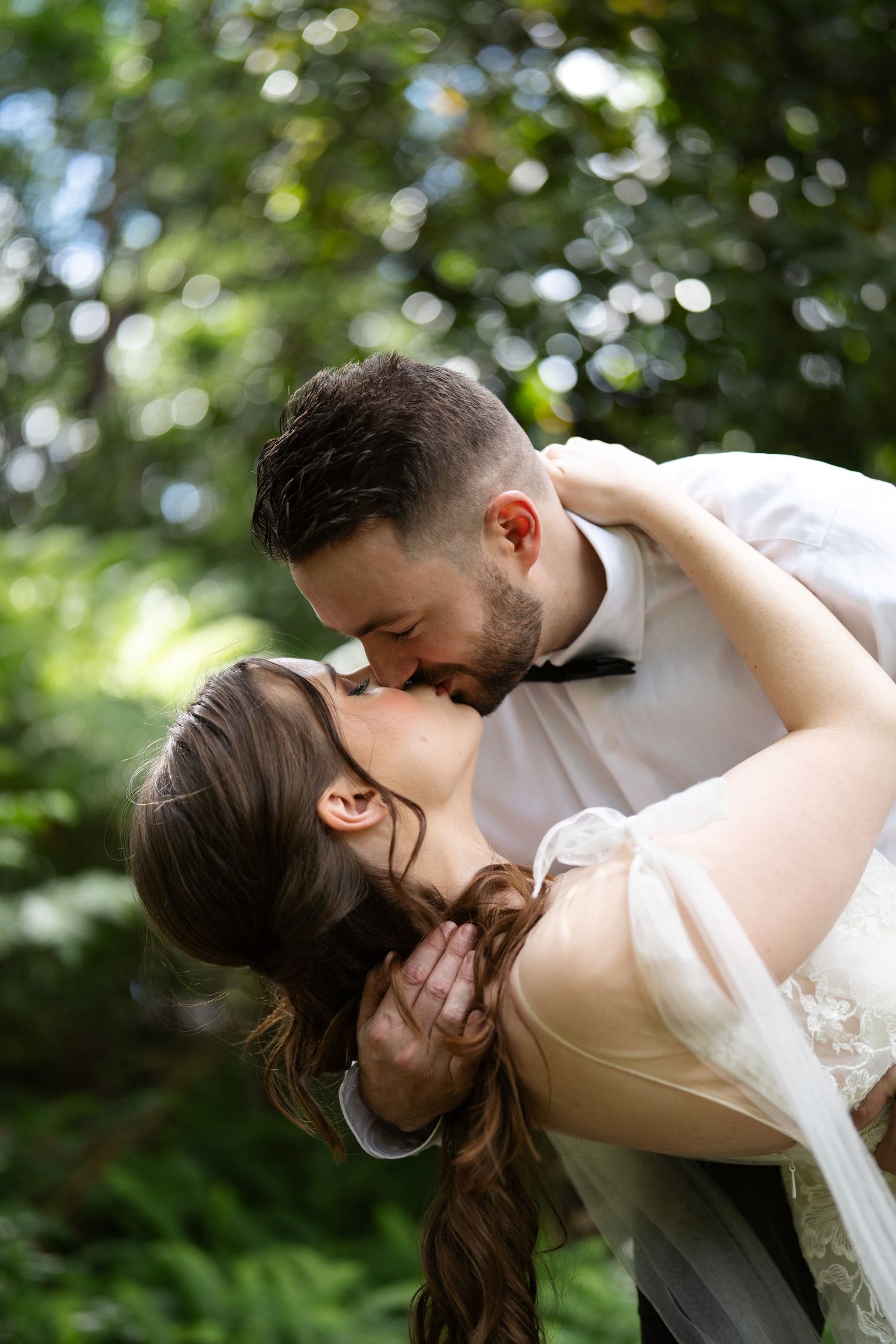 Groom dipping his bride for a kiss among green trees