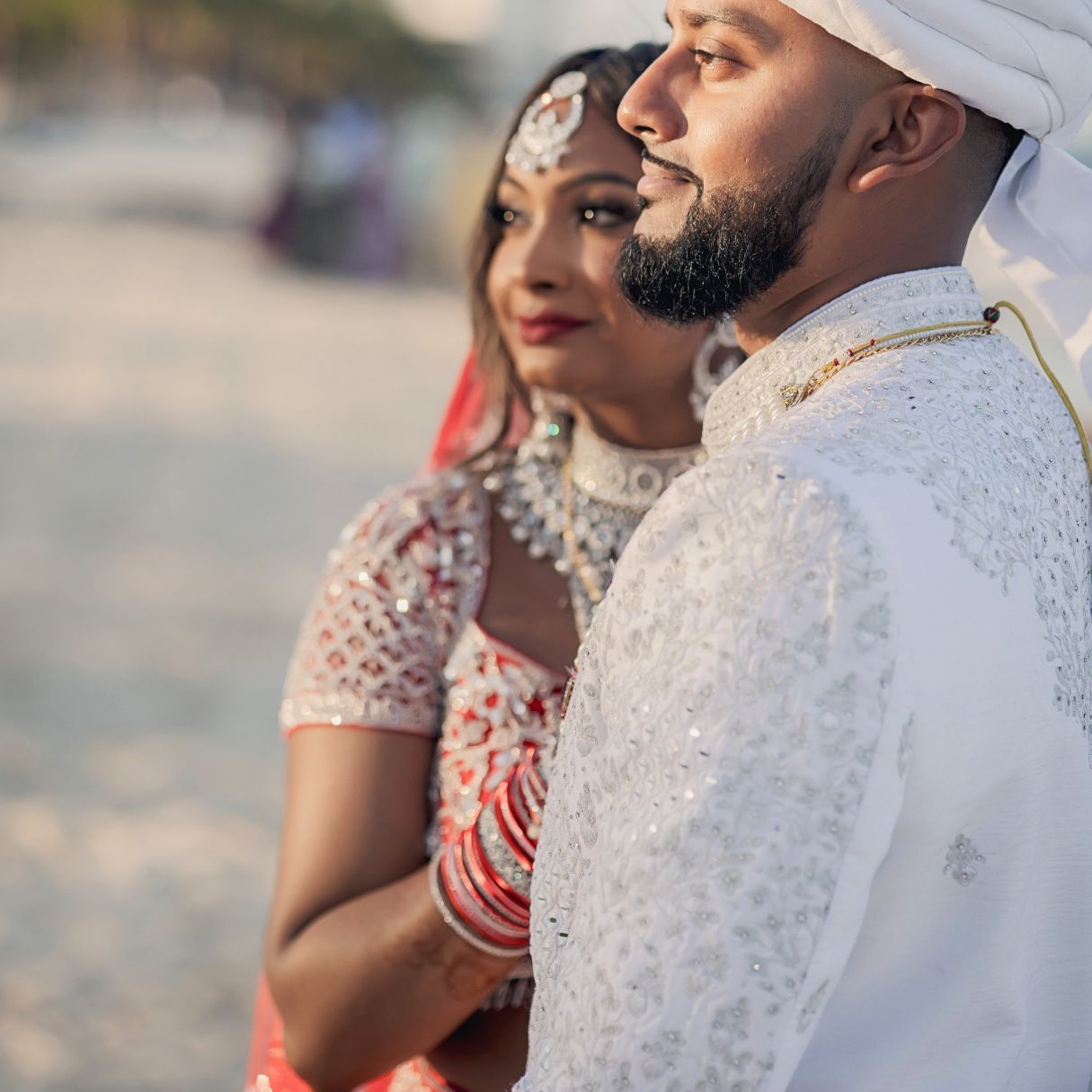 A couple in traditional Indian attire share a tender embrace, the woman smiling in gold jewelry and green outfit.
