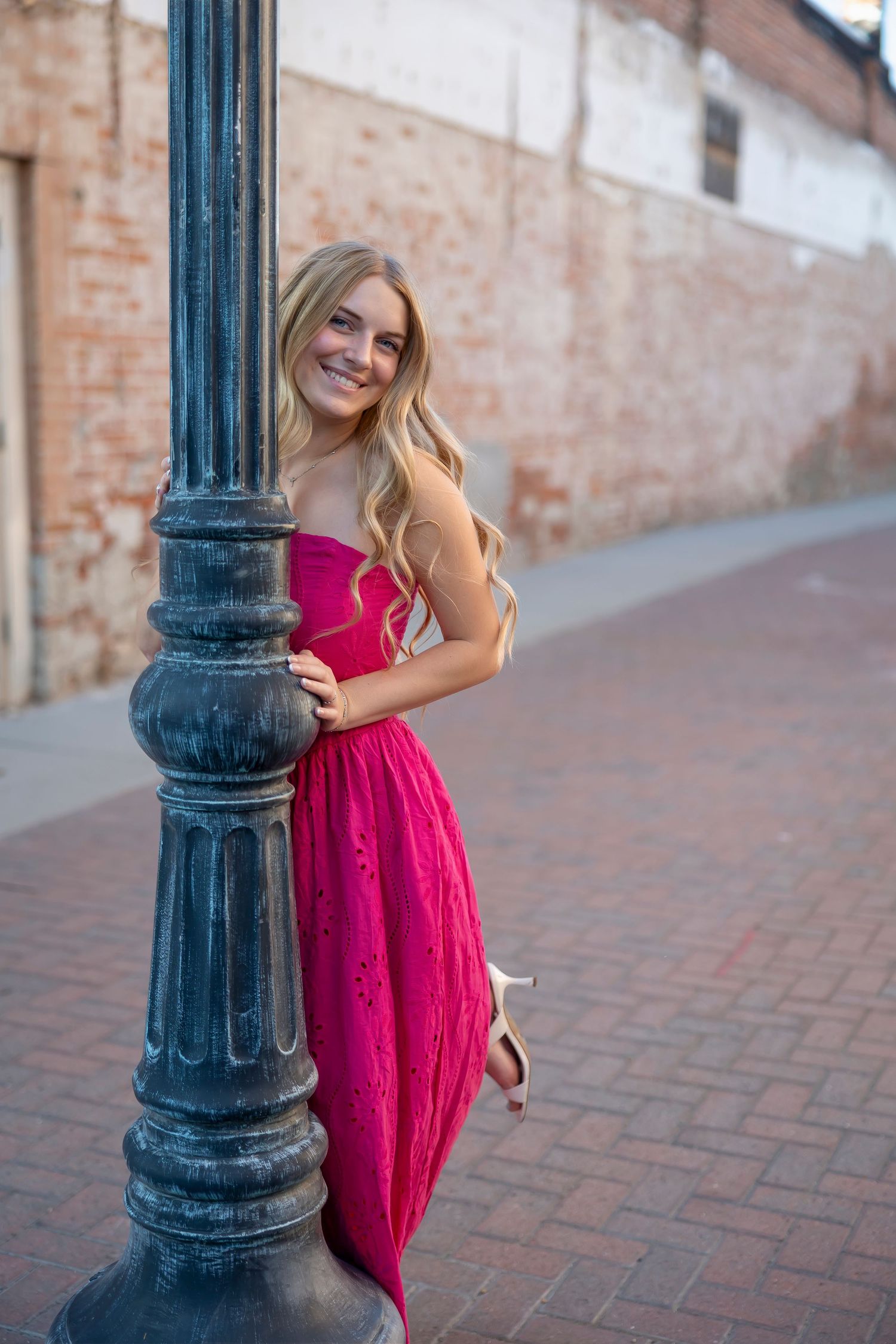 senior girl wearing pink dress leaning on lamp post