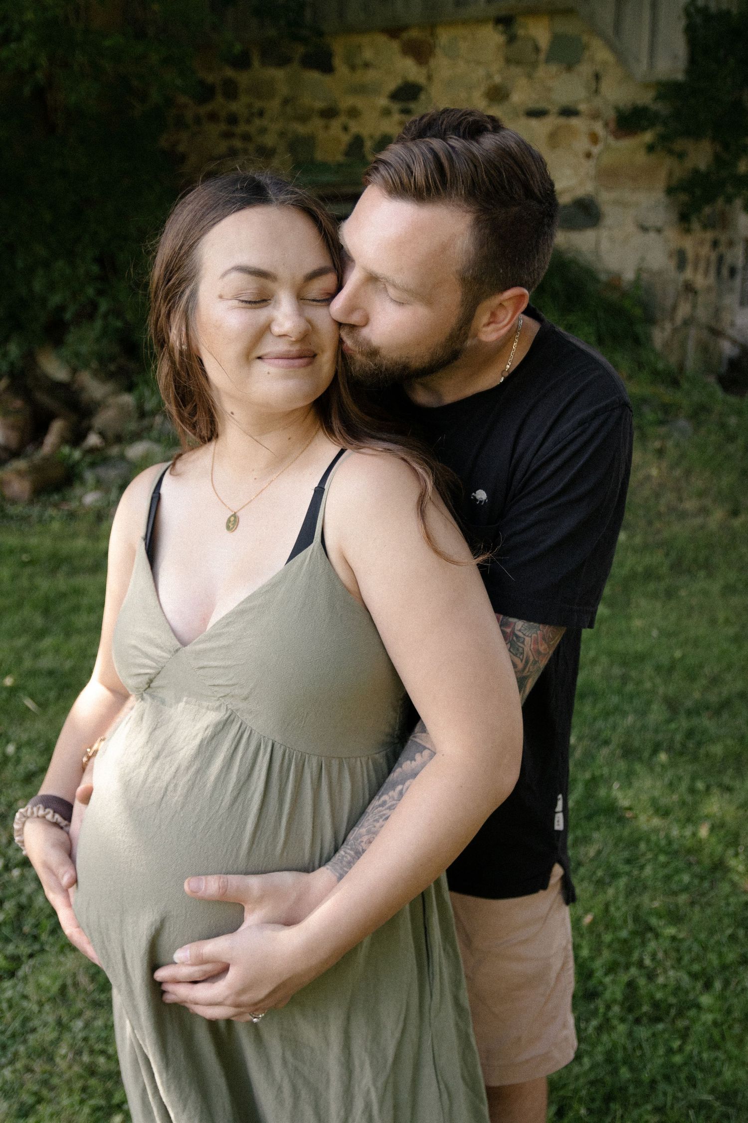 a couple kissing and cuddling holding the mother's belly during their maternity photoshoot