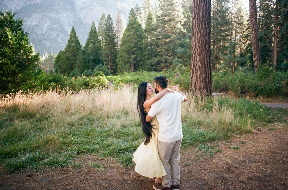 Couple embracing in a romantic outdoor setting with tall pine trees and mountains in Yosemite National Park.