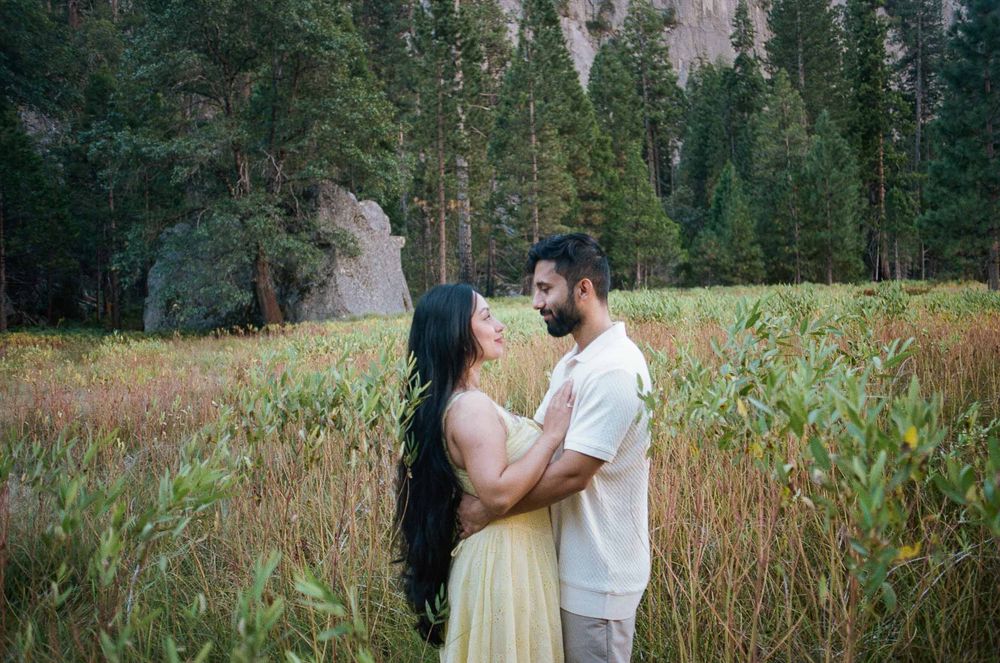 Couple sharing a romantic moment in a lush meadow surrounded by tall trees and rocky cliffs at Yosemite National Park.