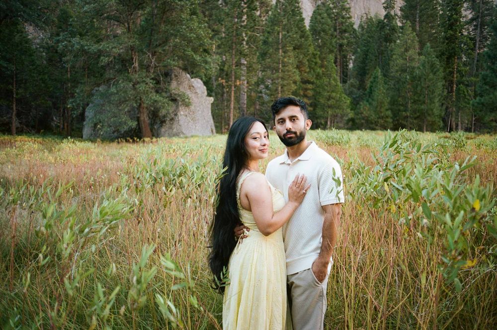 Couple standing in meadow, woman in yellow dress with long hair embracing man in cream shirt.