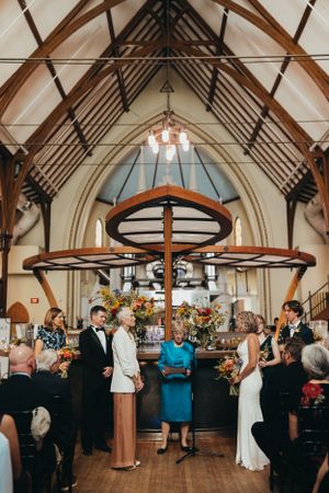 Wedding reception in a rustic church hall with exposed wooden beams and circular chandeliers.