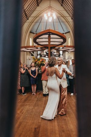 Wedding dance floor scene through doorway in historic church venue with wooden beams.