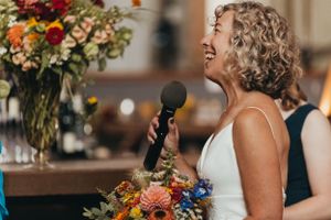 Colorful floral arrangements decorate wedding reception tables in rustic venue.