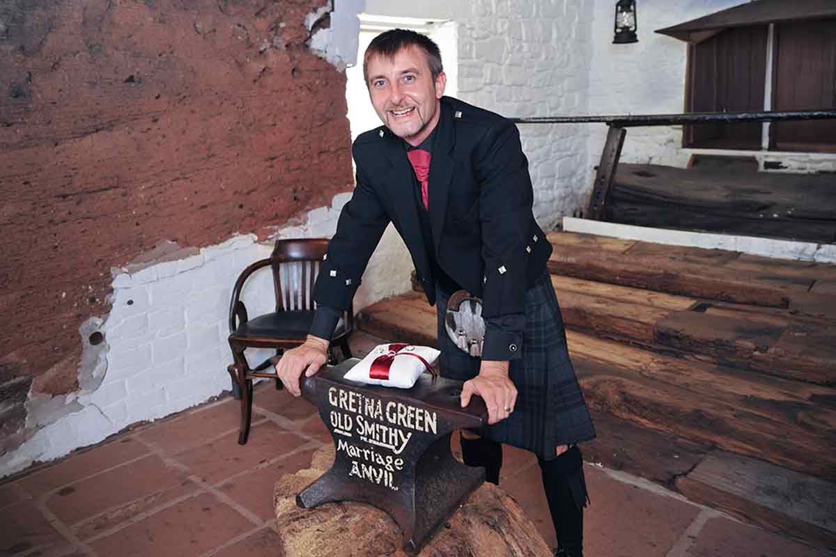 Man in Scottish kilt posing at Gretna Green Old Smithy famous anvil, traditional wedding venue in Scotland.