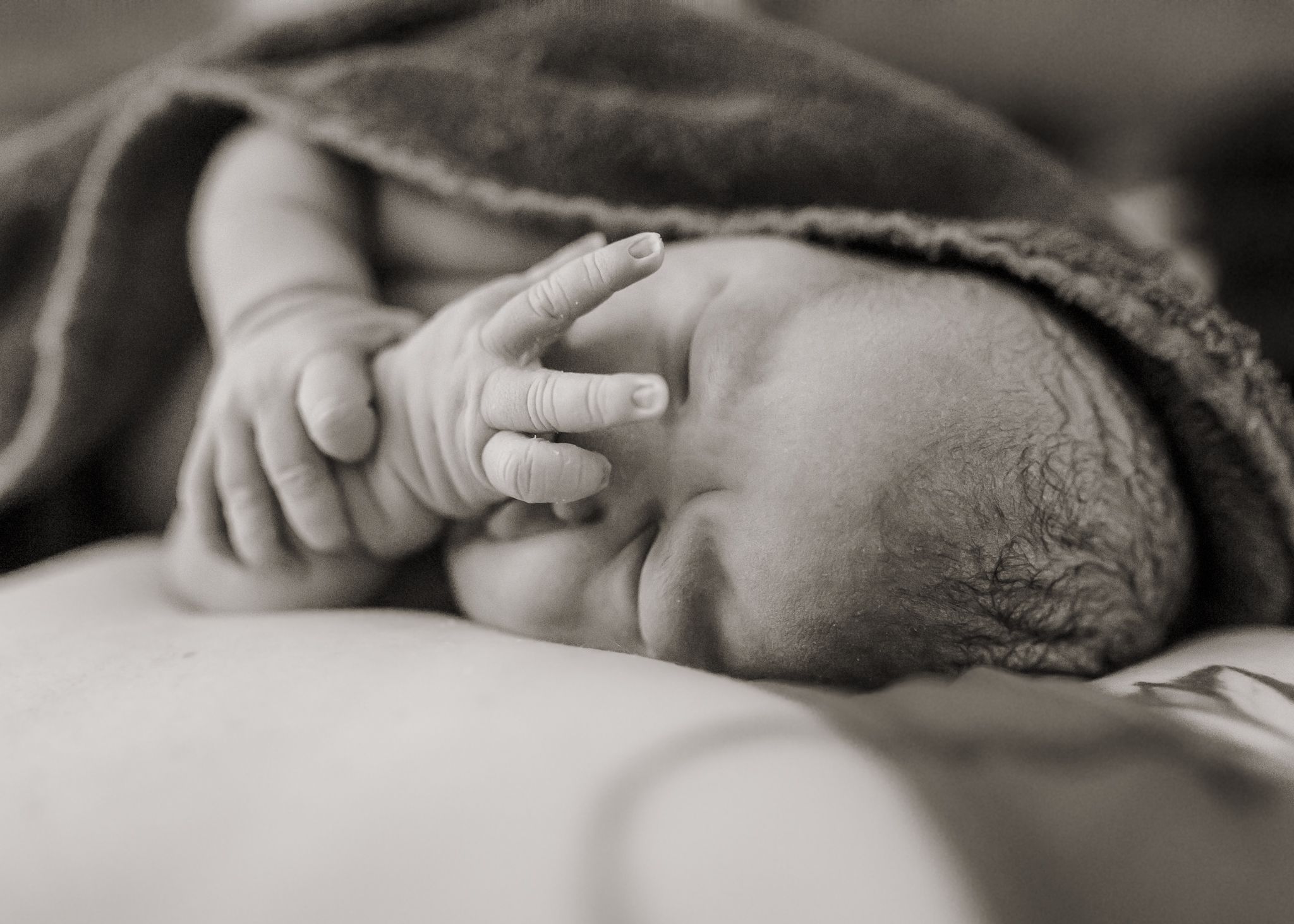 Black and white photo of a sleeping newborn baby wrapped in a blanket with tiny fingers visible.